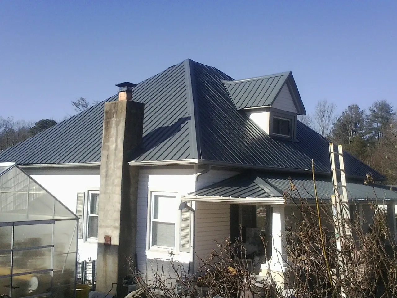 Dark blue standing seam metal roof on a white farmhouse with dormer — Slate & Tile Roof Repair by Roofing Brothers in Bancroft