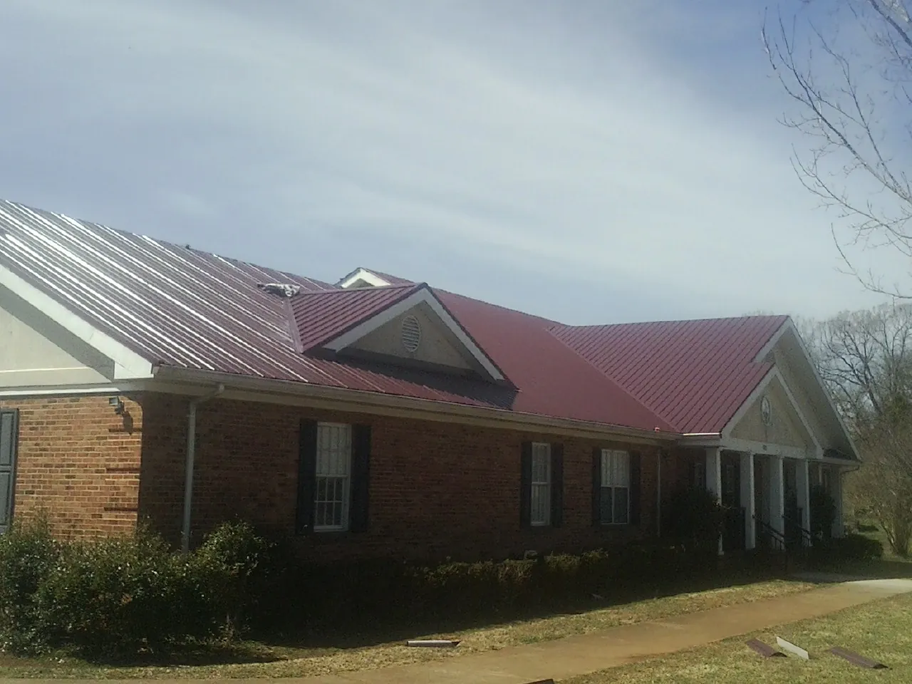 Red metal roof with gabled entries on a long brick building, from a Hail Damage Roof Repair job in Bancroft
