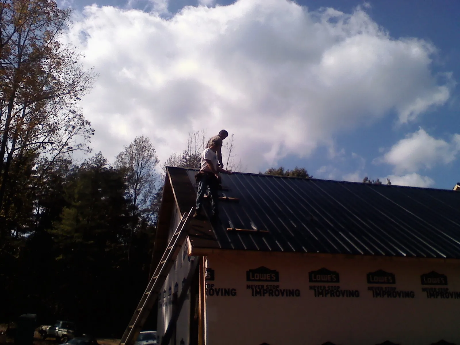 Roofer fastening dark metal panels high against a cloudy sky, from a Roof Inspection job in Bancroft